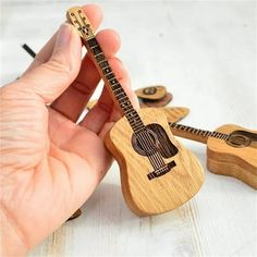 a hand holding a miniature guitar next to other wooden guitars on a white table top