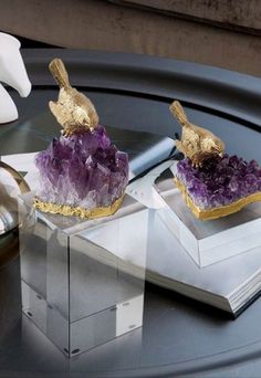 two pieces of jewelry sitting on top of a glass table next to white flowers and an open book