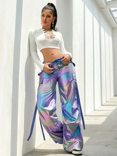 a woman standing next to a white wall with her hands on her hips and wearing colorful pants