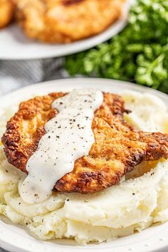 two white plates topped with mashed potatoes covered in gravy next to fried chicken