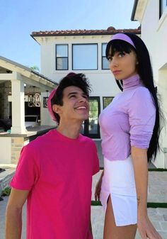 a man and woman standing next to each other in front of a house with a pink shirt on