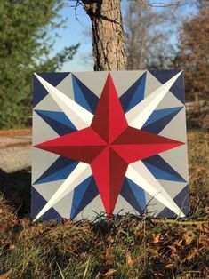 a red, white and blue star quilt sitting in the grass next to a tree