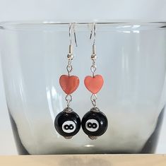 a pair of black and red heart shaped earrings on top of a glass bowl with a white background