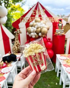 someone is holding up a popcorn box at an outdoor party with red and white decorations