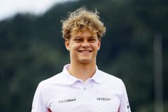 a young man with curly hair wearing a white polo shirt and smiling at the camera