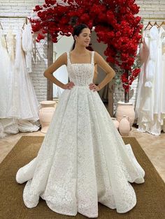 a woman standing in front of a dress on display at a bridal shop with red flowers behind her