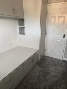 an empty room with white cupboards and carpeted flooring in front of a door