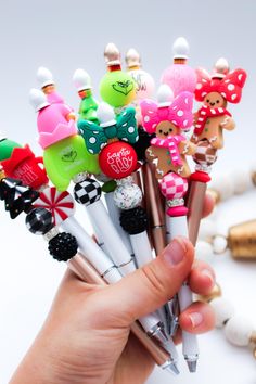 a hand holding a bunch of pens with different types of decorations on them in front of a white background