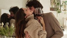 a man and woman kissing while holding wine glasses