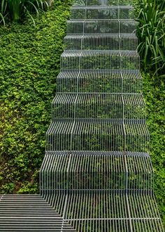 three metal cages are stacked on top of each other in front of green bushes and shrubbery