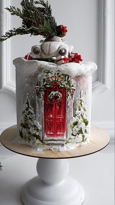 a decorated cake on a white pedestal with a red door and christmas decorations around it