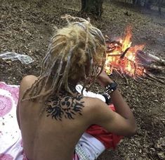 a woman with dreadlocks sitting in front of a campfire looking at something