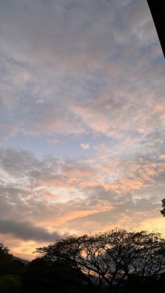 the sun is setting behind some trees and clouds