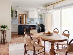 a dining room table with chairs and a bowl of fruit on it in front of an open kitchen door