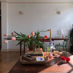 a wooden table topped with lots of books next to a vase filled with pink flowers