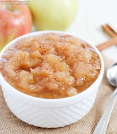 an apple pie in a white bowl with spoons next to it on a table