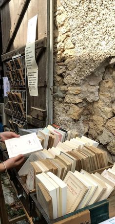 two women looking at books on a table in front of a stone building with signs hanging from it