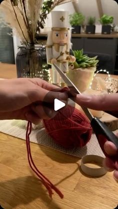 two hands are holding scissors and yarn on a table with other items in the background