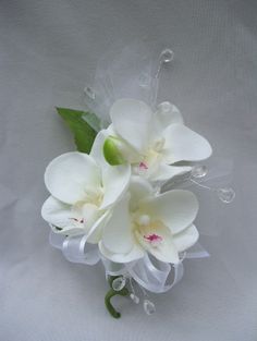 two white flowers with green stems on a white cloth covered surface, the centerpiece is made of glass beads and ribbon