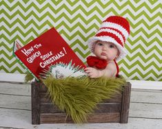 a baby wearing a red and white knitted hat sitting in a crate holding a book