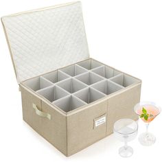 an open storage box with wine glasses and a glass next to it on a white surface