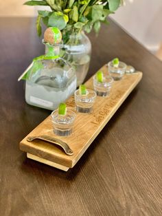 three shot glasses sitting on a wooden tray next to a vase with flowers in it