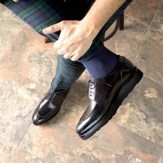 a man in black dress shoes and green plaid socks sitting on a chair with his foot up