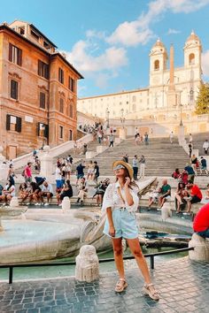 a woman standing in front of a fountain with lots of people sitting on the steps