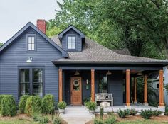 a blue house with wooden porches and pillars on the front door is surrounded by greenery