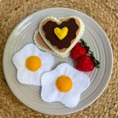 two fried eggs on a plate next to strawberries and heart shaped cookie cutters