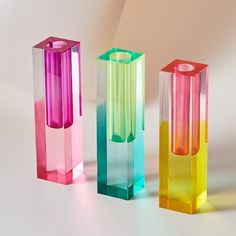 three different colored vases sitting next to each other on a white surface with shadows