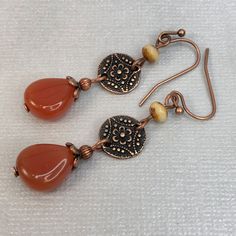 Carnelian color glass teardrop beads dangle gracefully from copper discs.  Whether you're dressing up for a special occasion or looking to add a touch of sophistication to your casual outfit, these dangle earrings are sure to make a statement. Handcrafted with care, these Carnelian Teardrop Dangle Earrings are a must-have accessory for any jewelry lover. Hypoallergenic ear wires (nickel and lead free). Choose ear wire style at checkout. Artisan glass beads produced in small quantities in the Cze Brown Czech Glass Teardrop Earrings, Handmade Czech Glass Teardrop Earrings, Rust Teardrop Handmade Jewelry, Brown Teardrop Czech Glass Jewelry, Brown Czech Glass Teardrop Jewelry, Vintage Copper Teardrop Earrings, Artisan Teardrop Copper Earrings, Nickel-free Teardrop Vintage Beaded Earrings, Vintage Teardrop Beaded Earrings Nickel Free