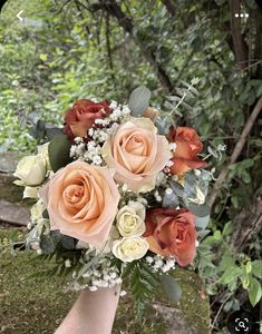 a bouquet of roses in someone's hand with greenery and trees in the background