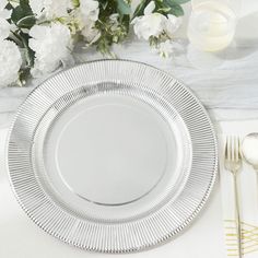 an empty plate on a white table cloth with flowers and silverware in the background