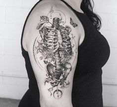 a woman with a skeleton and flowers tattoo on her arm is standing in front of a white brick wall