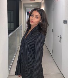 a woman standing in an office hallway wearing a pinstripe blazer and heels