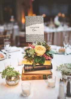 a table topped with lots of books covered in flowers and greenery next to candles