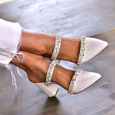 a woman's legs wearing white high heels with crystal embellishments on them