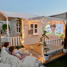 two people sitting on a couch in front of a house with christmas lights around it