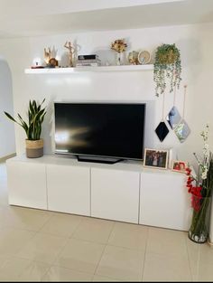 a flat screen tv sitting on top of a white entertainment center next to potted plants