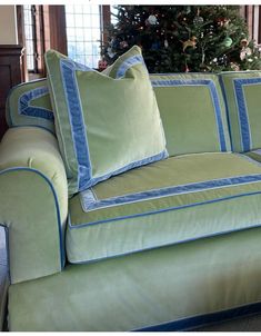 a green couch sitting in front of a christmas tree with blue trimming on it