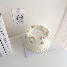 a white cake sitting on top of a table next to two books and a pen