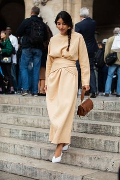 a woman is walking down some steps wearing a tan dress and white shoes with her handbag