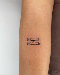 a woman's arm with two small fish tattoos on the back of her left arm