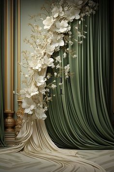 a tall white flower arrangement in front of a green curtain