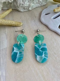 two blue and green earrings sitting on top of a wooden table next to a starfish shell