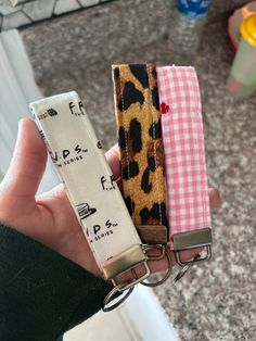 a person holding three different types of keychains in their hands, one has a leopard print and the other has a pink checkered ribbon