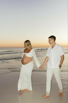 a pregnant couple holding hands and walking on the beach at sunset, with their belly wrapped around each other