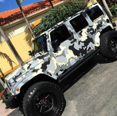 a camouflage jeep is parked in front of a building with palm trees on the side