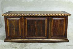 an old wooden chest with carvings on the top and bottom, sitting against a white wall